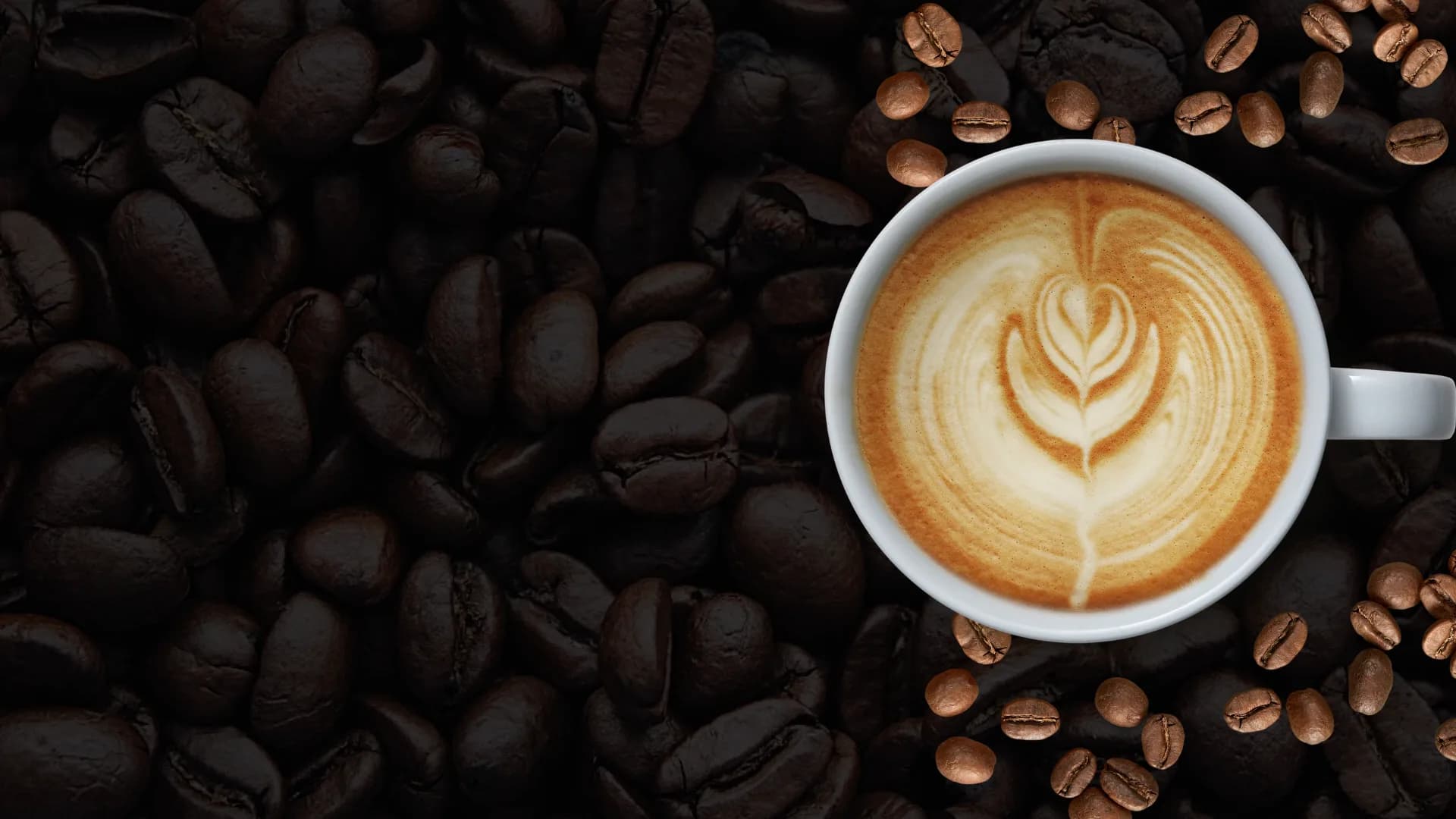 Latte art in a white cup surrounded by roasted coffee beans