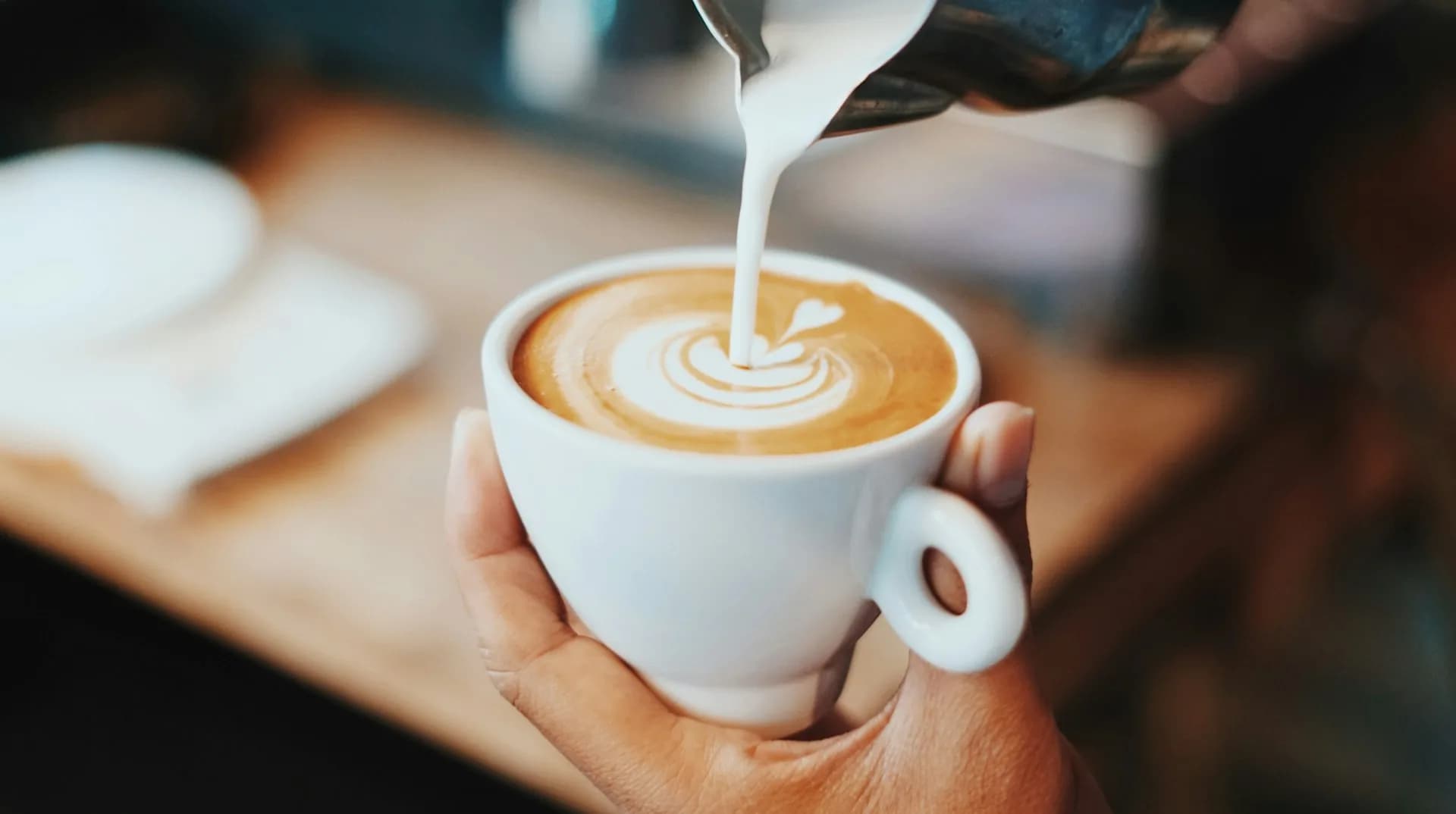 Person pouring latte art into a cup